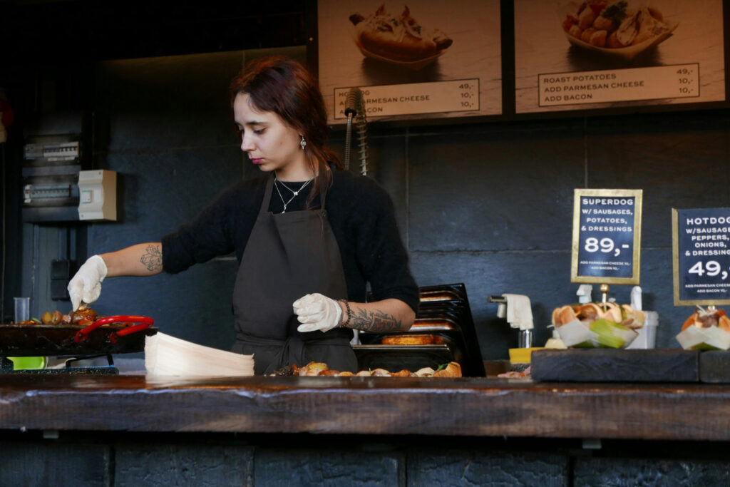 Staff member wearing plastic gloves grilling fresh vegetables behind the counter.